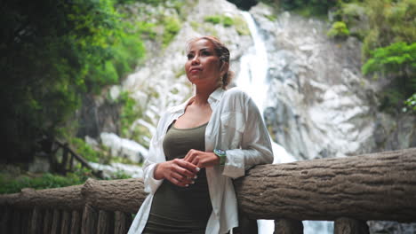 una mujer asiática está de pie frente a una majestuosa cascada, disfrutando de la belleza natural y la atmósfera pacífica.
