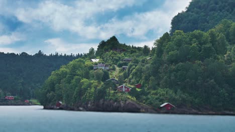 miniaturized tidy red wooden cabins and boathouses scattered along the forest-covered fjord coast
