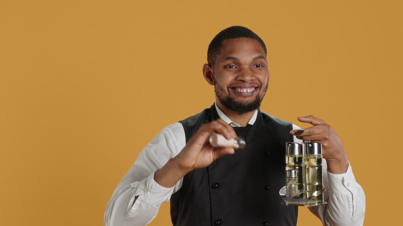 Smiling friendly waiter pouring down salt from the salt shaker on the cruet set