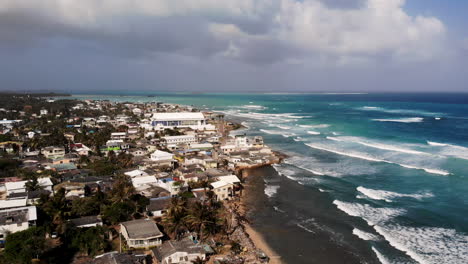 Vista-Aérea-De-Un-Pueblo-Costero-Con-Olas-Azules-Rompiendo-En-La-Costa