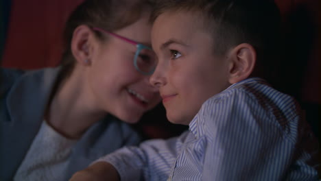 girl whispering to boy watching movie in cinema. child movie entertainment