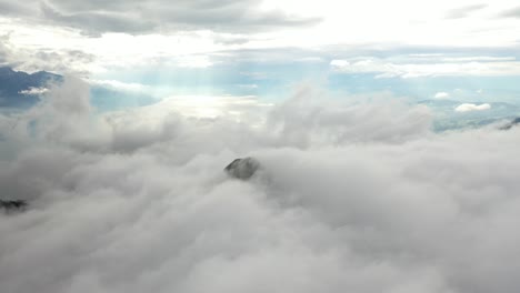 disparo de dron moviéndose hacia adelante, revelando la cima de una montaña que apenas se asoma a través de las nubes que se mueven rápido, pasando