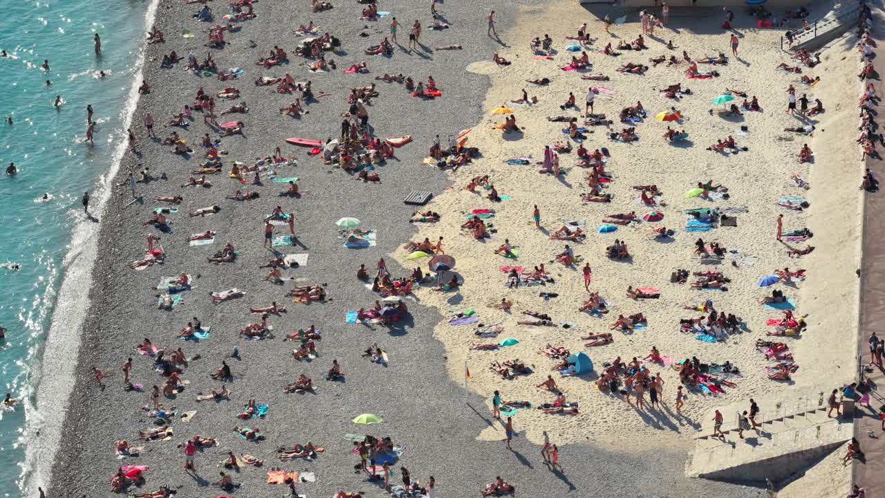 Aerial drone view of a busy section of Nice beach with umbrellas, swimmers, and promenade walkway, Nice, France