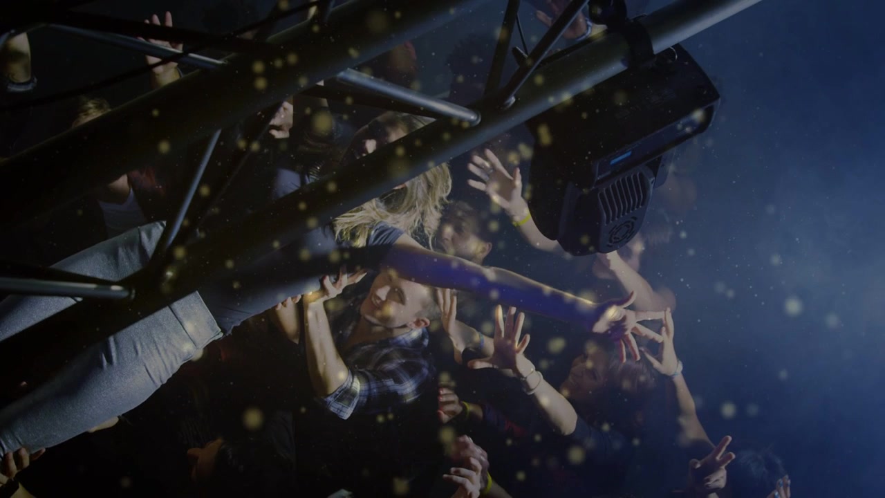 Blonde concertgoer leaning over barrier, reaching toward stage as light flaring, crowd steadying