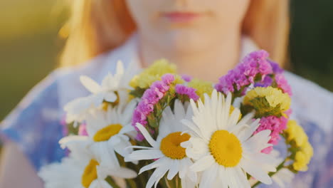 blonde girl holds a bouquet of flowers stands in a meadow at sunset