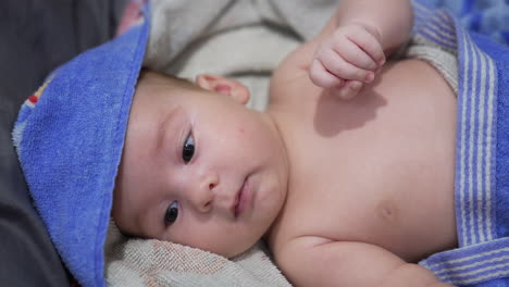 lovely baby resting wrapped in towel after a bath. sweet infant child opening little mouth and shoving tiny fists. close up.