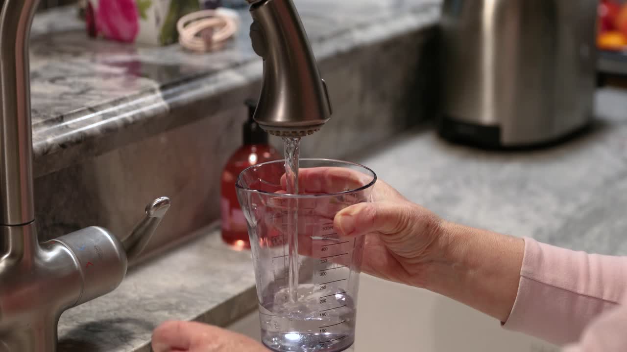 mujer llenando una taza con agua en la cocina en 4k
