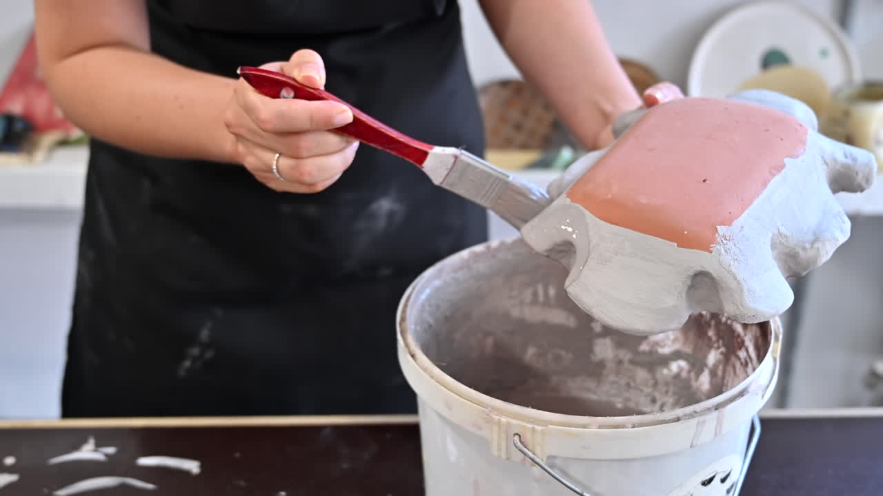 Donna che dipinge un piatto arancione di argilla con il colore bianco