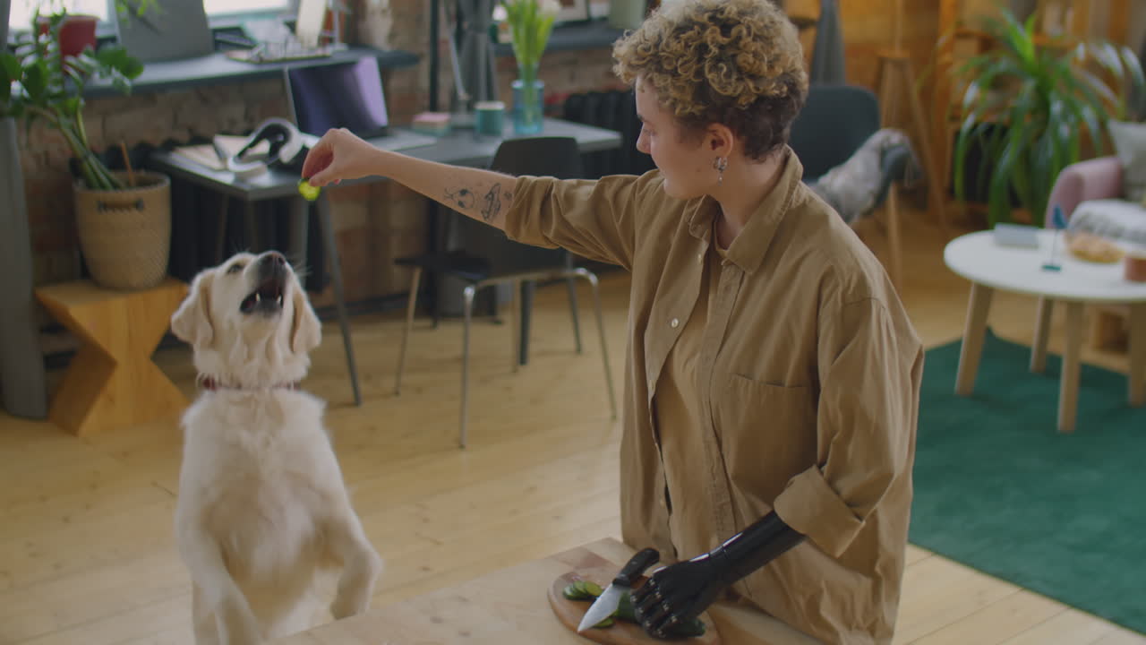 Woman with Prosthetic Arm Treating Dog while Cooking Food at Home