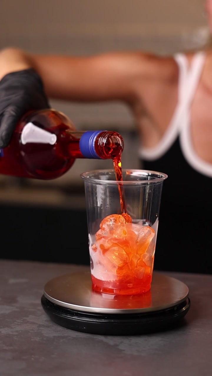 Barman che versa un aperitivo rosso in un bicchiere di plastica con ghiaccio