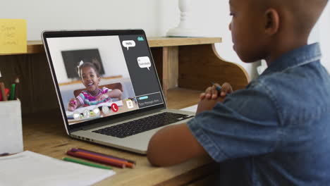 african american boy having a video call with classmate on laptop at home