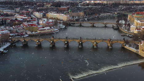 Aerial-view,-light-snowfall-on-Prague,-Czech-Republic,-Charles-bridge-and-Vltava-river-on-winter-day,-drone-shot