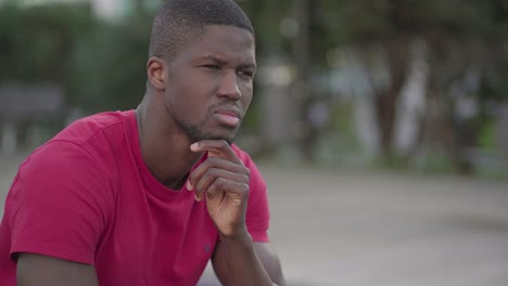 man sitting in park, touching chin, looking around, thinking