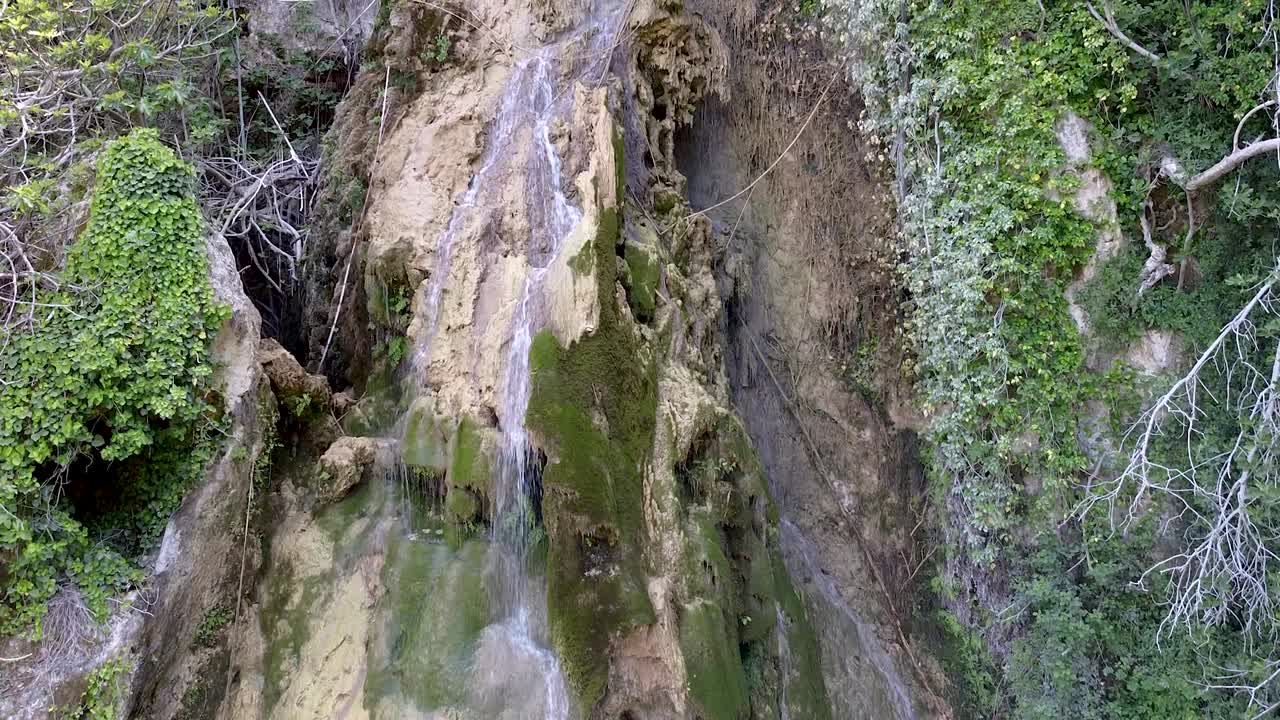 Explore the stunning view of a hidden waterfall surrounded by lush greenery. The clear water cascades over moss-covered rocks, creating a peaceful atmosphere