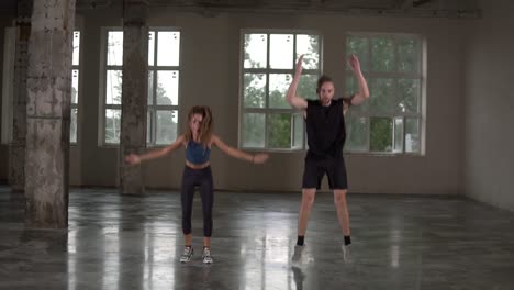 man and woman with dreadlocks in fitness studio doing exercises together, performing push ups with jumps and claps. loft interior. front view