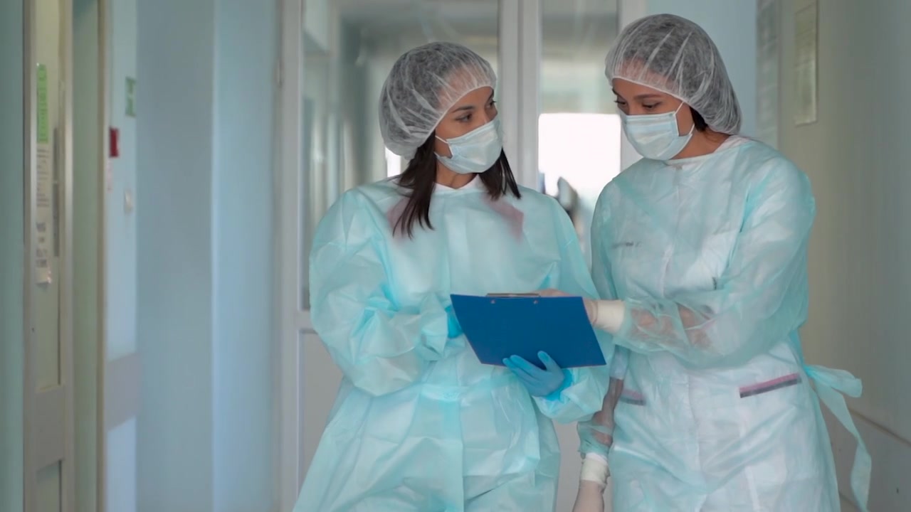 Dokter dan Perawat Wanita Berjalan Melalui Rumah Sakit Sambil Mendiskusikan Diagnosis dan Perawatan Pasien