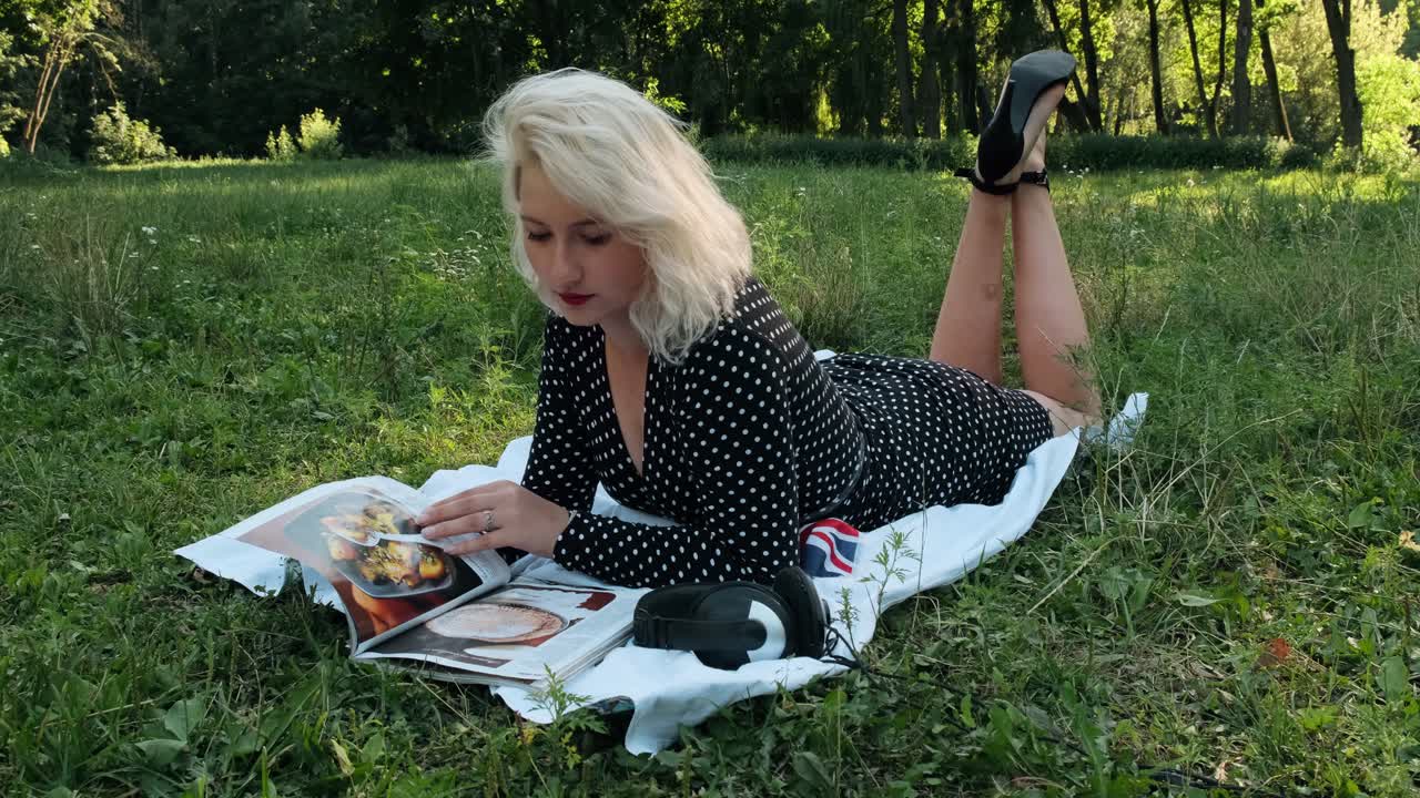 hermosa chica en el parque hojea una revista.