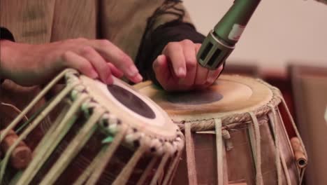 medium close up of a mans hands tapping out a rhythm on a pair of tabla drums