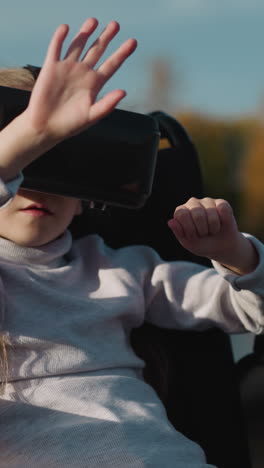 preschooler girl with legs injury plays computer game using vr glasses. small child waves hands controlling character actions on at sunset closeup