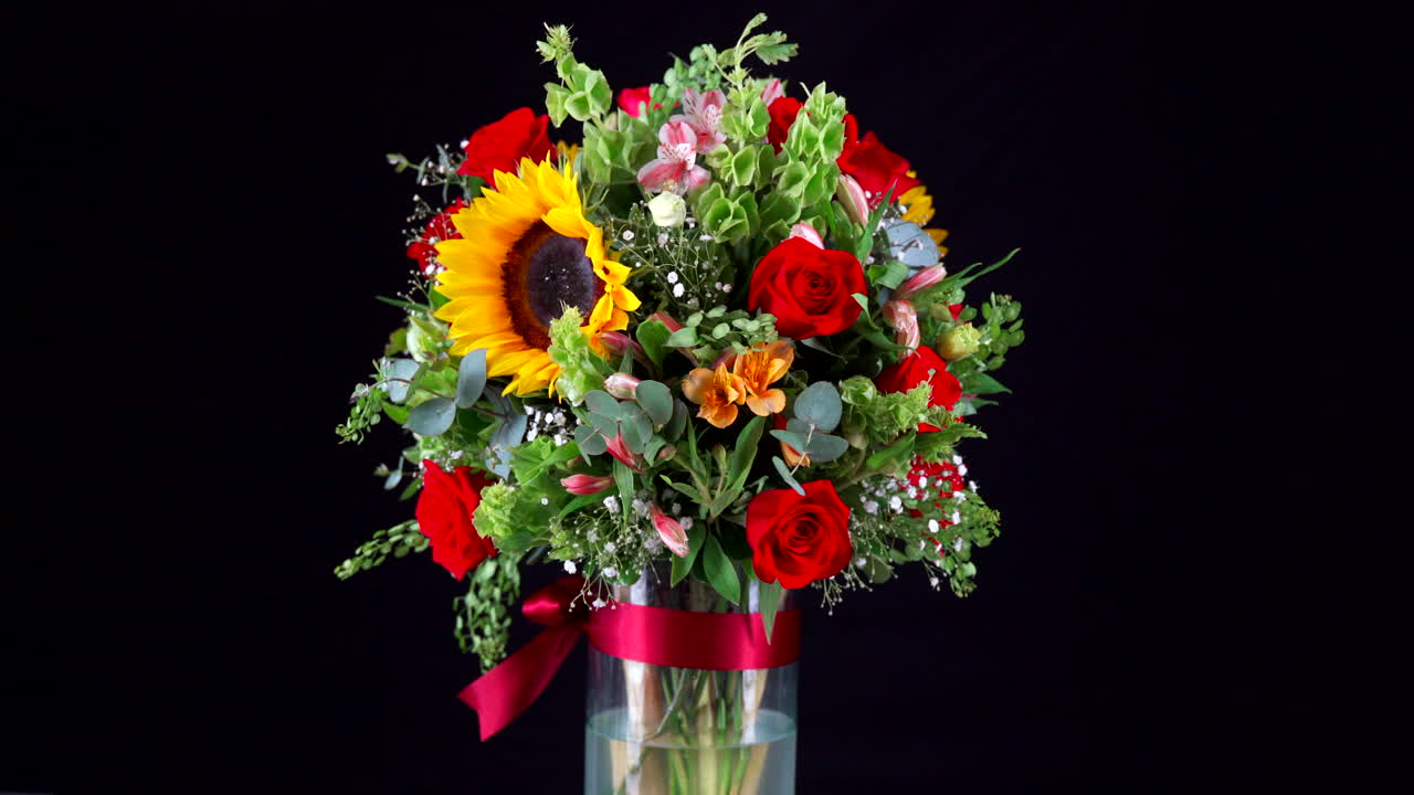 Vaso di rose e girasoli che ruota su sfondo nero, inquadratura media.