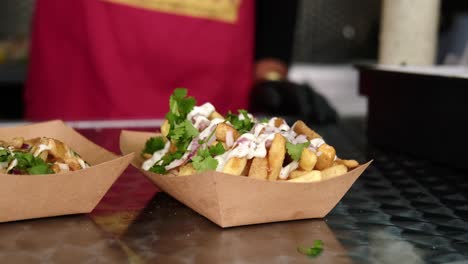 close up of chef dropping spices and condiments on top of warm french fries inside food truck at festival.