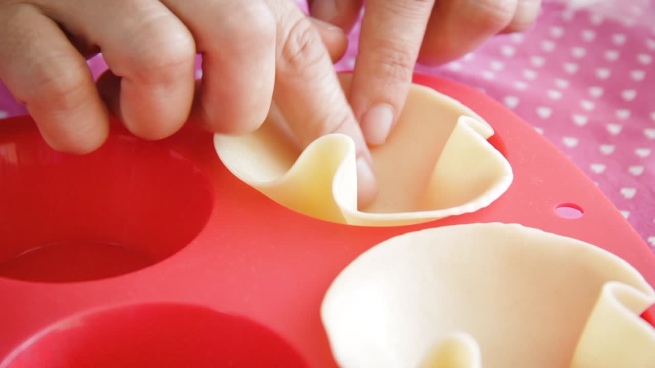 Frauenhände legen rohen Teig in eine pastellrote Silikon-Muffinbackform.