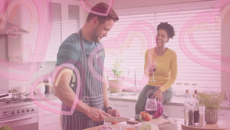 animation of hearts over diverse couple cooking together and drinking wine in kitchen at home