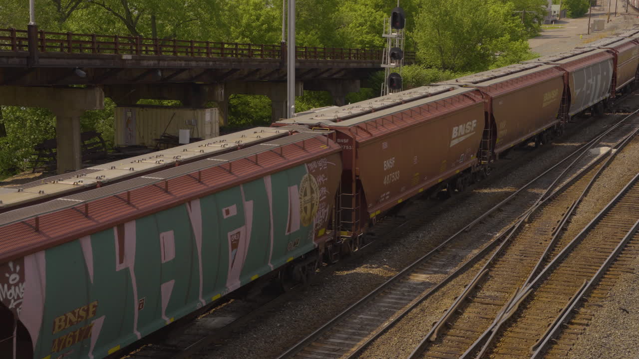 Vagoni ferroviari si muovono lentamente sui binari davanti a un vecchio ponte arrugginito a Youngstown, Ohio, in un pomeriggio di sole.
