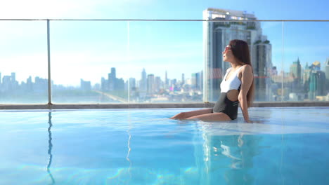 gorgeous asian woman sitting in rooftop swimming pool with stunning bangkok city skyline