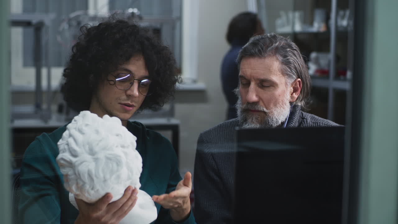 Two men collaborating on a project involving a sculpture and a laptop