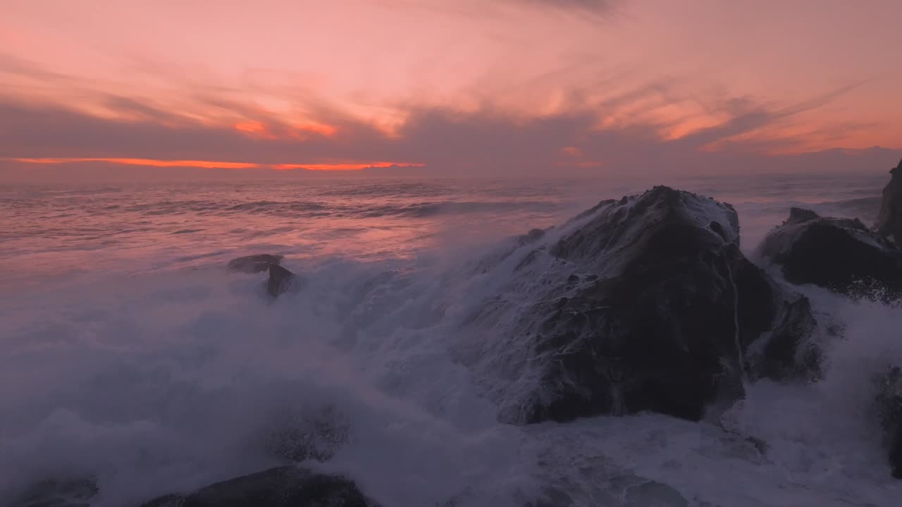 colores vívidos de la puesta de sol con algunas olas feroces chocando contra las rocas