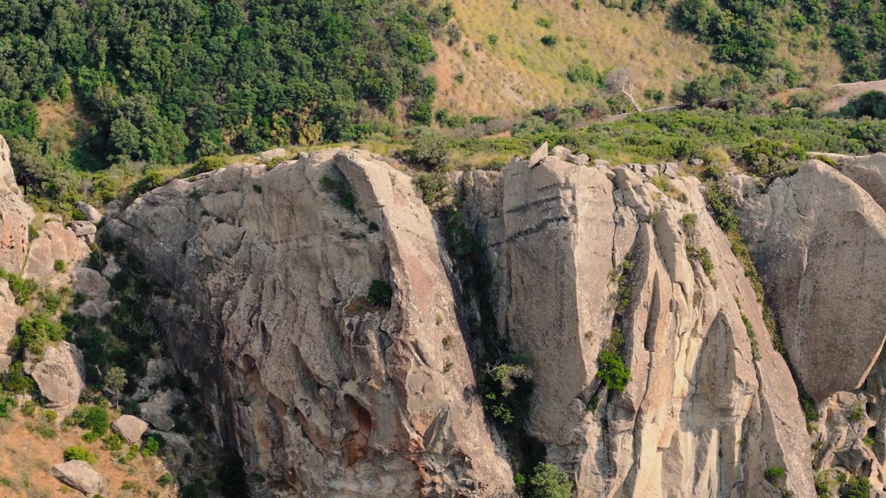 Tebing batu pasir yang terkikis dengan semak-semak di lereng bukit hijau