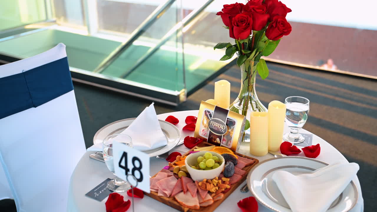 Mesa de jantar romântica posta para dois no convés de um navio de cruzeiro. Close-up da mesa com rosas vermelhas, velas, aperitivos e o fundo da Ponte de Manhattan em Nova York ao pôr do sol.