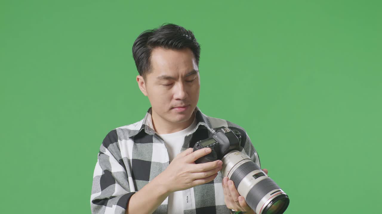 카메라에서 사진을 보는 아시아 사진작가의 클로즈업은 스튜디오에서 녹색 스크린 배경에 서서 손을 흔들고 있습니다.