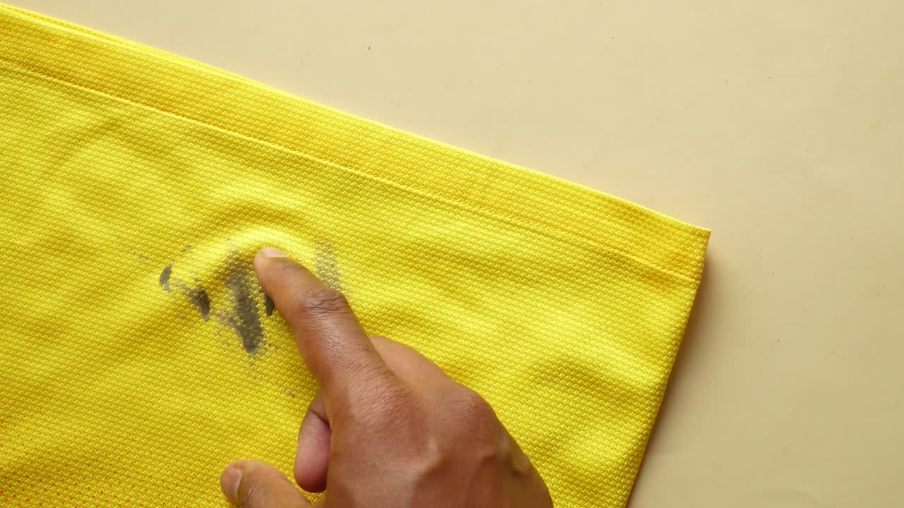 A person's hand cleaning a dirty stain on a yellow shirt.