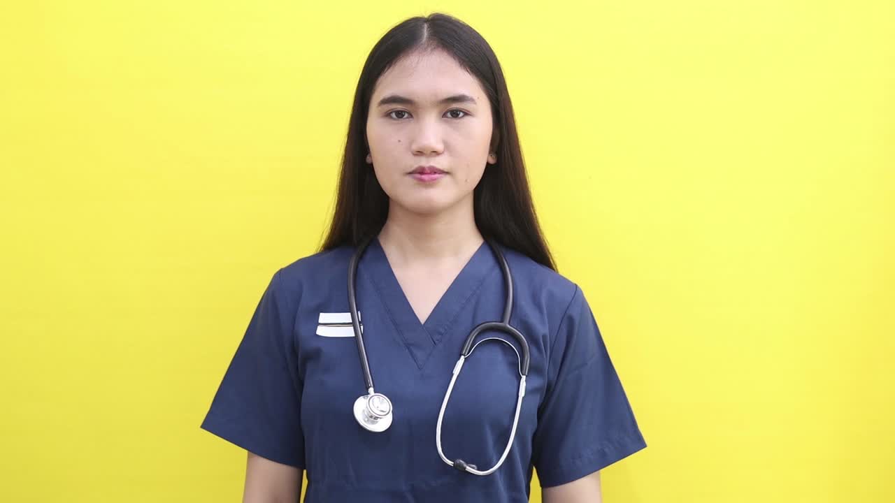 Smiling happy young Asian doctor woman pointing fingers down on workspace area copy space mock up isolated on yellow background studio portrait