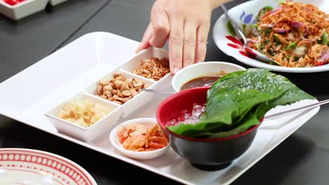 hands assembling traditional thai miang kham leaf wraps with ingredients