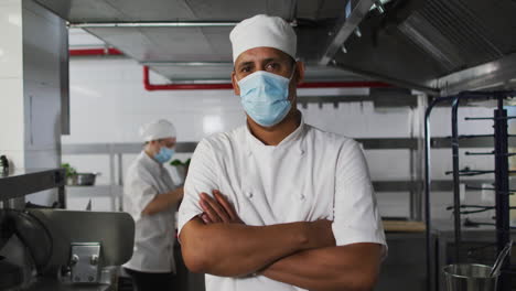 Portrait-of-mixed-race-male-chef-wearing-face-mask-with-arms-crossed