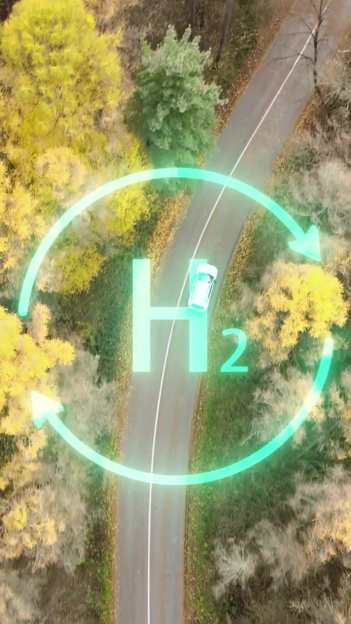 Video verticale di un'auto bianca autonoma alimentata a idrogeno che guida lungo una strada autunnale con animazione di energia verde H2, a simboleggiare una fonte di energia pulita e futuristica