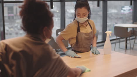 colleagues disinfecting table in restaurant