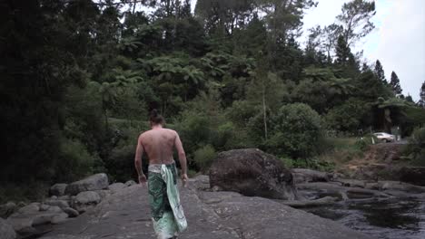 man walking on rocks by river in forest
