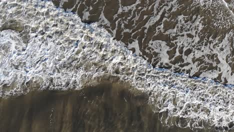aerial, top down, drone shot panning above waves at a beach, on langeoog island, in north germany
