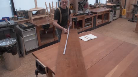 woodworker measuring dimensions of lumber on workbench with measuring tape