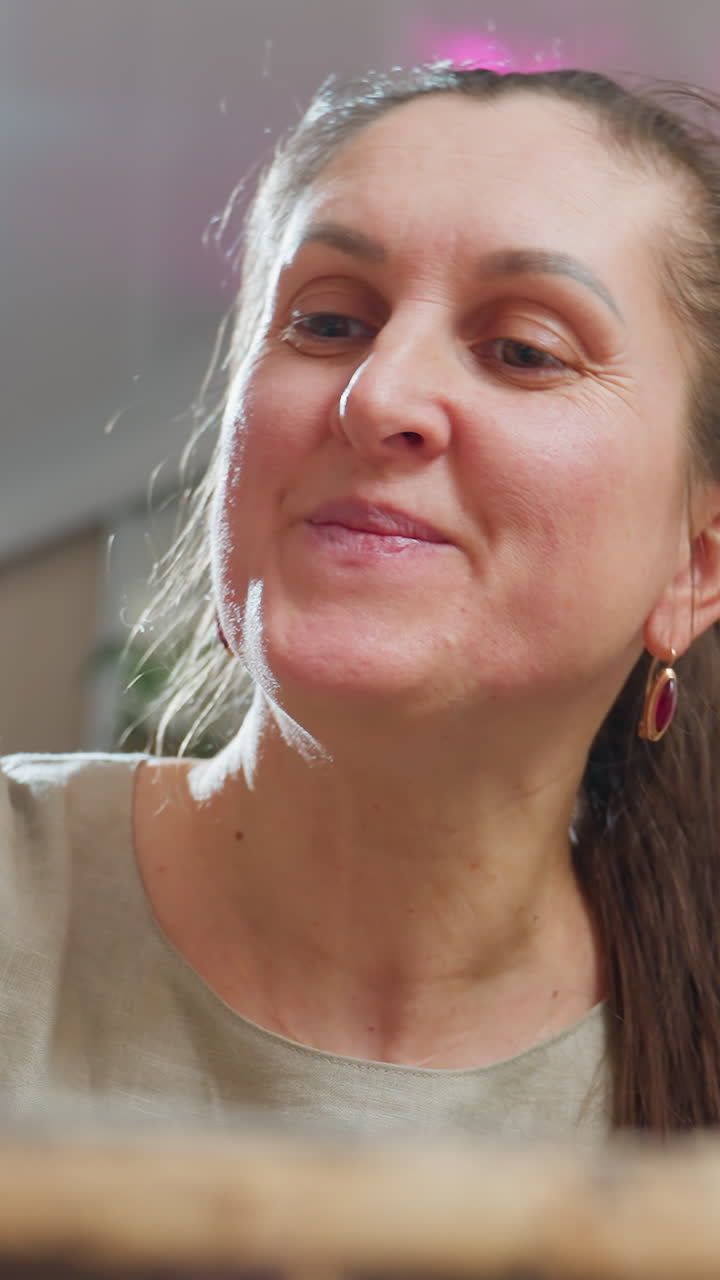 Mujer caucásica decorando un pastel con manos firmes y una sonrisa dulce, luz ambiente rosa, trazos de glaseado suaves, concentración total, detalles del postre visibles, ambiente festivo en la cocina