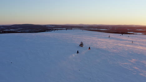 Pair-of-snowmobile-riders-speeding-across-Norbotten,-Swedish-snow-covered-landscape-at-sunrise