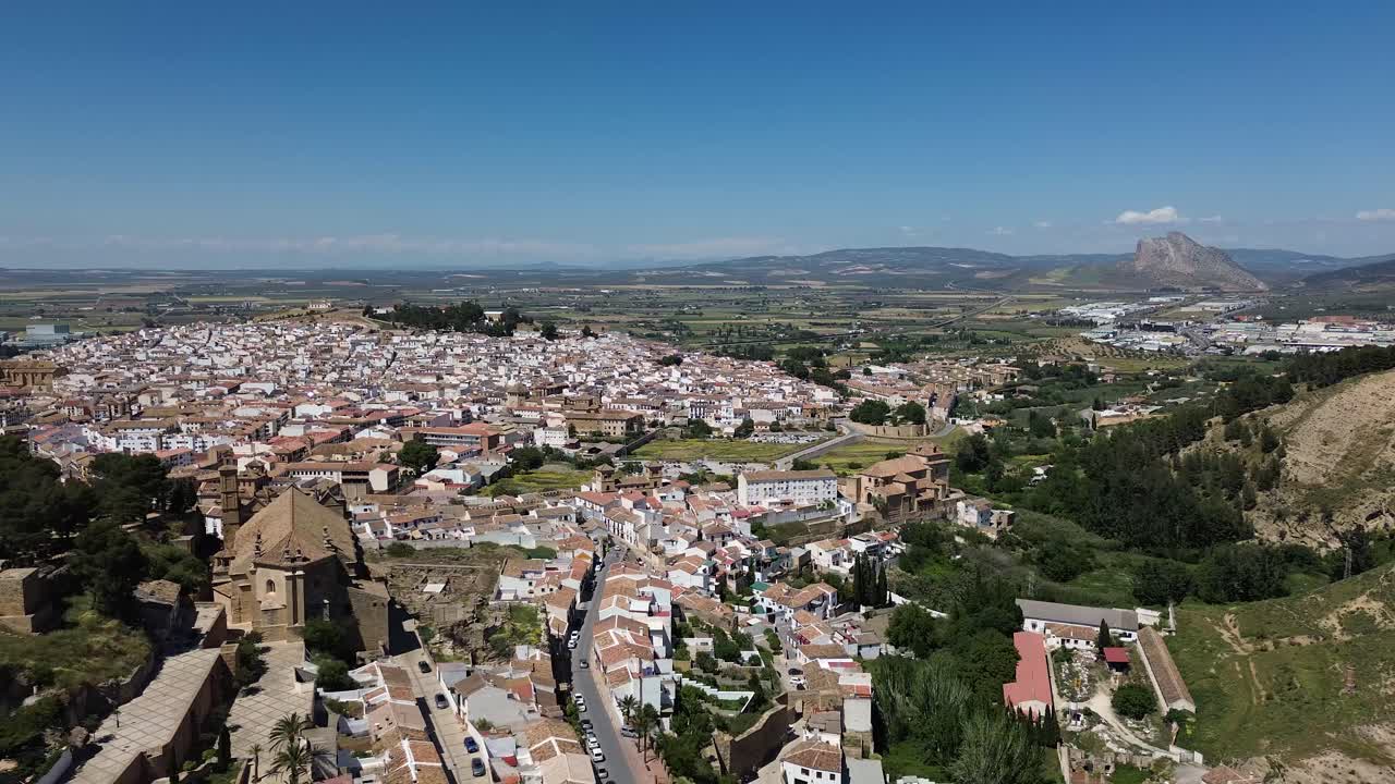 aerial drone footage flying over Antequera in soain under bright blue skies, revealing the perfect blend of historic architecture, lush surroundings, and mountain backdrops.