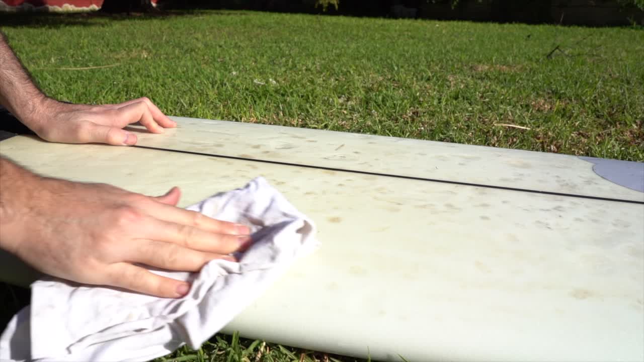 The hands of a surfer cleaning his board in the garden