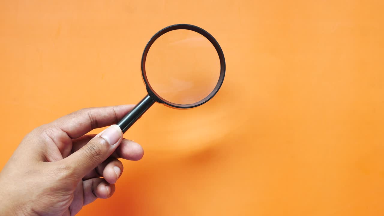 Hand Holding a Magnifying Glass on an Orange Background