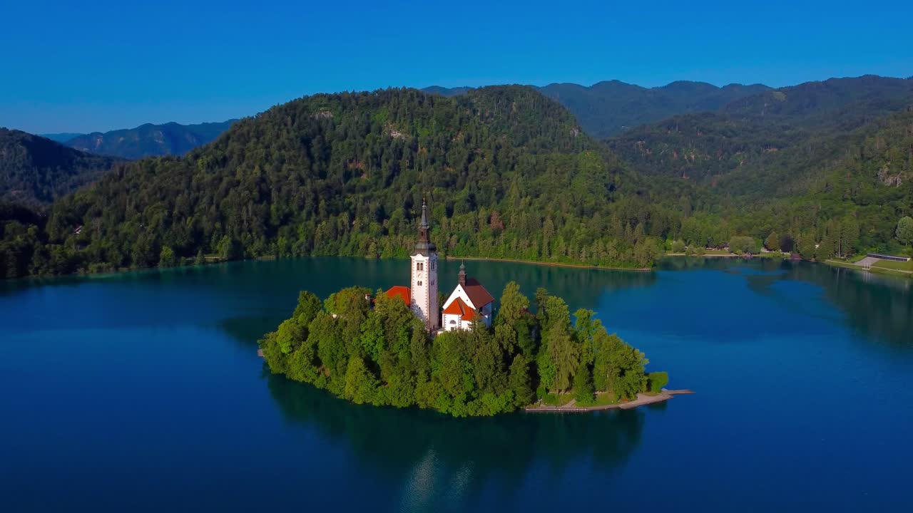 Circling around the famous and iconic island of Lake Bled with mountains covered in forest in the background - Slovenia