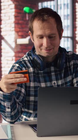 vertical video happy man excited to do online shopping, typing debit card information on laptop